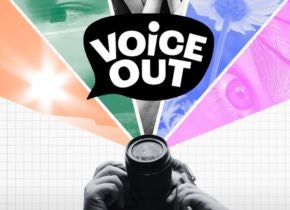 A person holding a camera looks upward toward a graphic design that features elements of art and design.