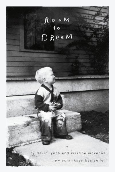 Black and white photo of a young child laughing sitting on a stoop in front of a house.