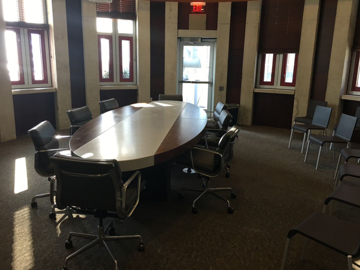 Room with very large oval table with chairs all around it and some chairs lining the walls. 
