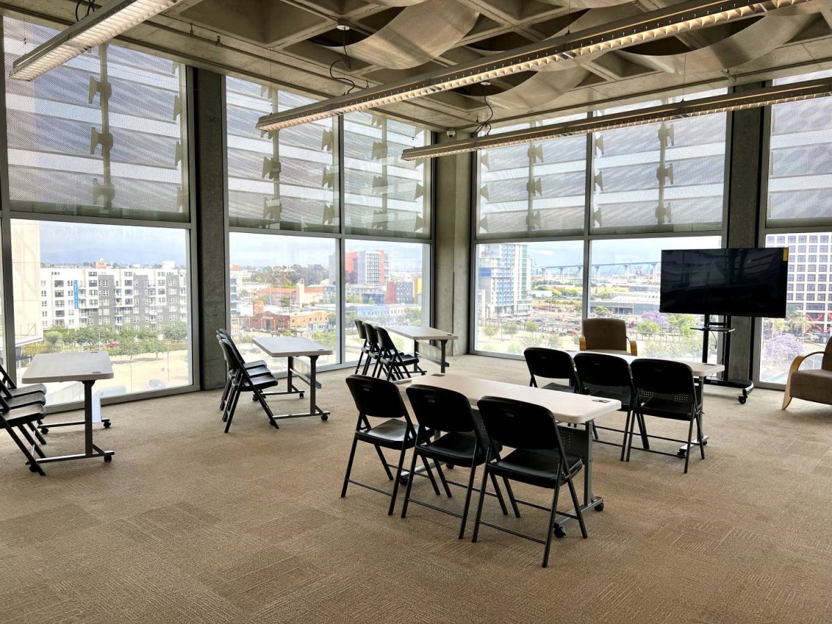 Room with glass windows around, set up classroom style with a rolling T.V. In front