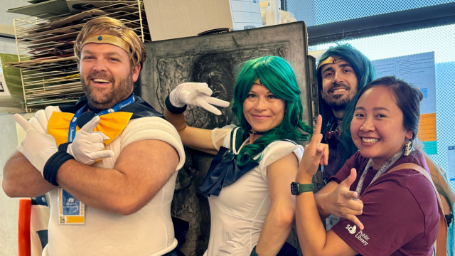 A woman and two men dressed as anime characters with colorful bows and wigs pose with an IDEA Lab staff member in the Lab. 