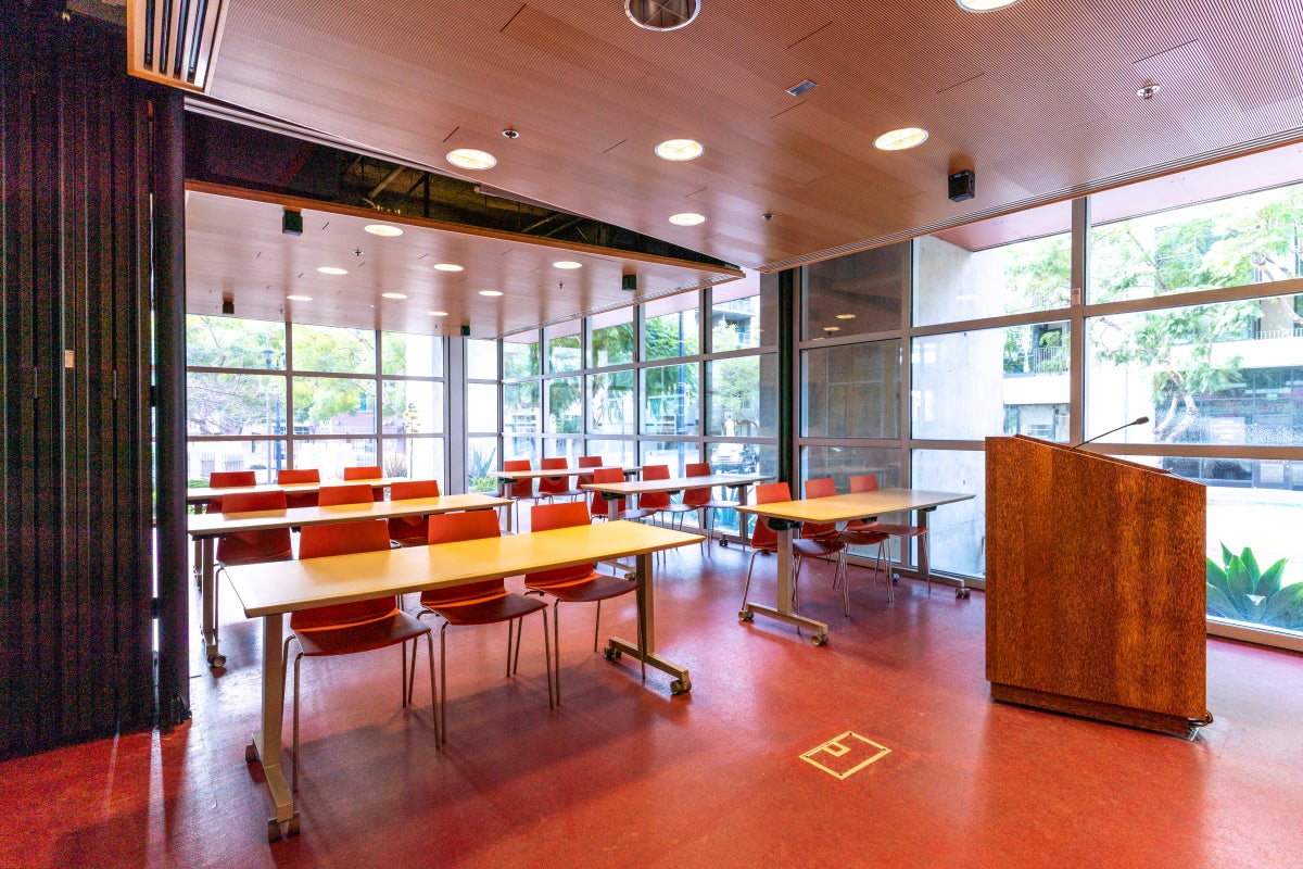 Classroom with desks, chairs, a podium and floor-to-ceiling windows. 