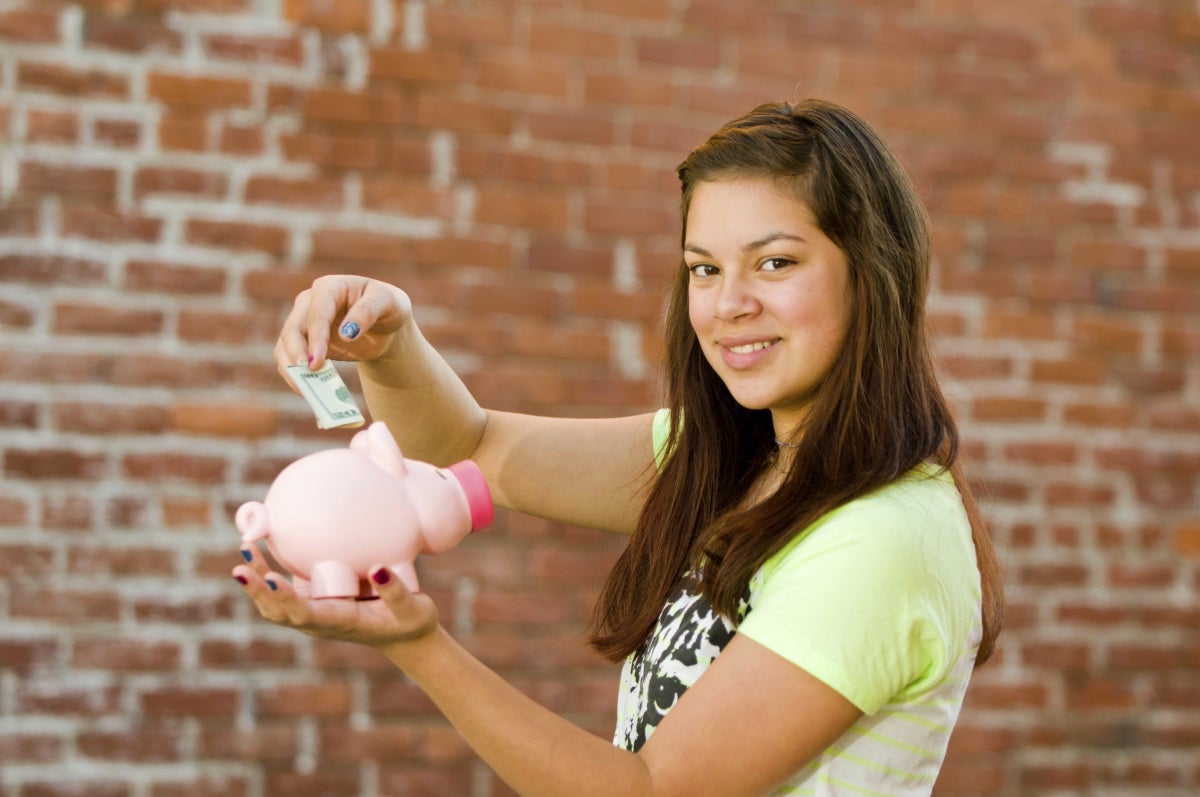 Youth holding a pink piggybank with one hand and money on the other. 