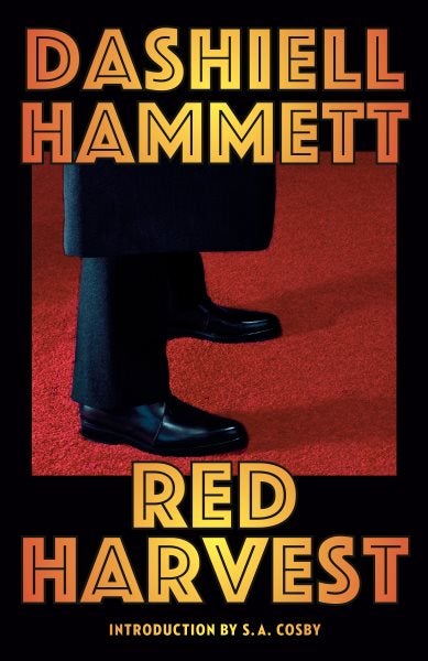 Cover of the novel Red Harvest by Dashiell Hammett. The cover features an illustration of the lower legs of a suited figure, standing on red carpet. The book title and author’s name are in bright orange block text.