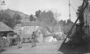 Man in full western gear and teenage boy walking past horse-drawn wagons at the Campo Ranch&#44; undated [c. 1870-1896]