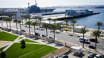 A bayside street lined with palm trees with a docked Navy vessel in the background
