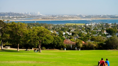 Two people sit on grass in a park overlooking San Diego