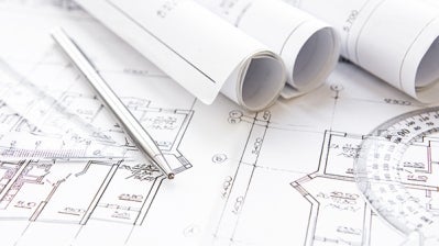 Rolled sheets of paper plans along with a pen and protractor on top of unrolled plans