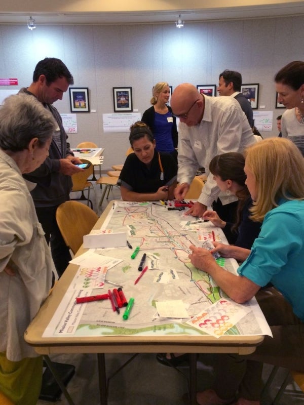 A group of 6 people at a table community mapping. Papers and writing supplies are on the table.