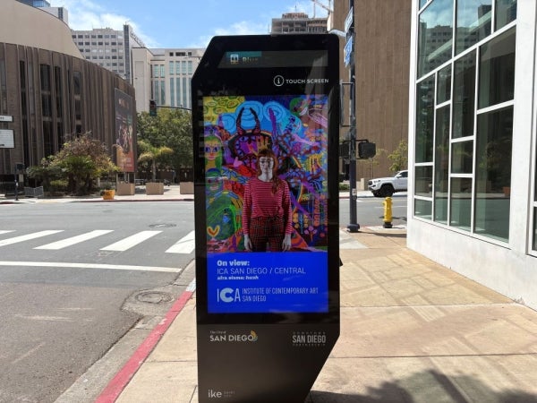An digital information kiosk on the sidewalk. The kiosks displays the Institute of Contemporary Art San Diego's ad.