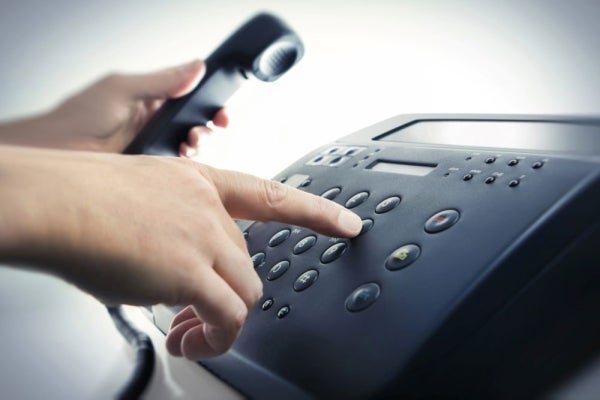 A person's hands press a button on a phone keypad and holds a phone. The phone system is black.