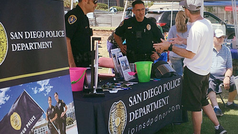 person speaking with two police staff at a SDPD booth