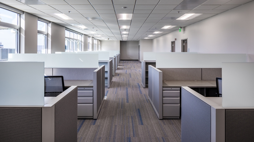 inside of an office with the aisle down the middle and two rows of cubicles lined up 