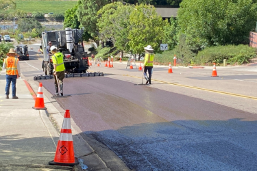 three workers slurry sealing a section of a street, surrounded by trees