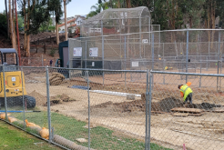 construction worker digging dirt surrounded by a chain fence and baseball field