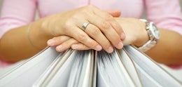 Photo of Hands Folded over a Row of Binders