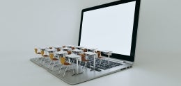 Desks and chairs on top of a laptop keyboard simulating a virtual classroom setting. 