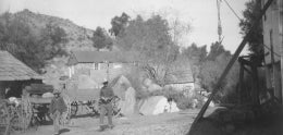 Man in full western gear and teenage boy walking past horse-drawn wagons at the Campo Ranch&#44; undated [c. 1870-1896]