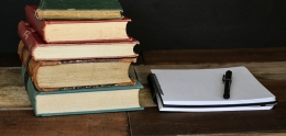 Stack of books next to a notepad and pen