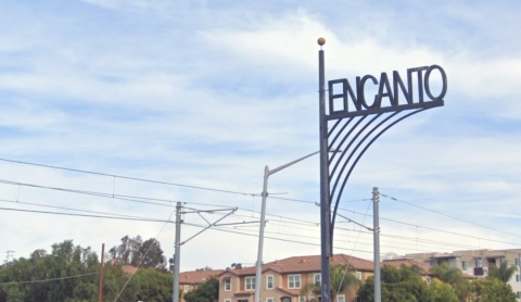 Ornamental street sign that says "Encanto" with neighborhood in background